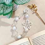 Pearl bracelet with a white flower charm on a beige surface with an open book and decorative elements.