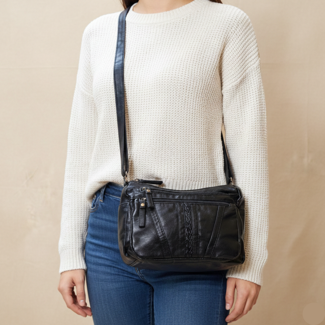 Person wearing a black leather crossbody bag with a plain background