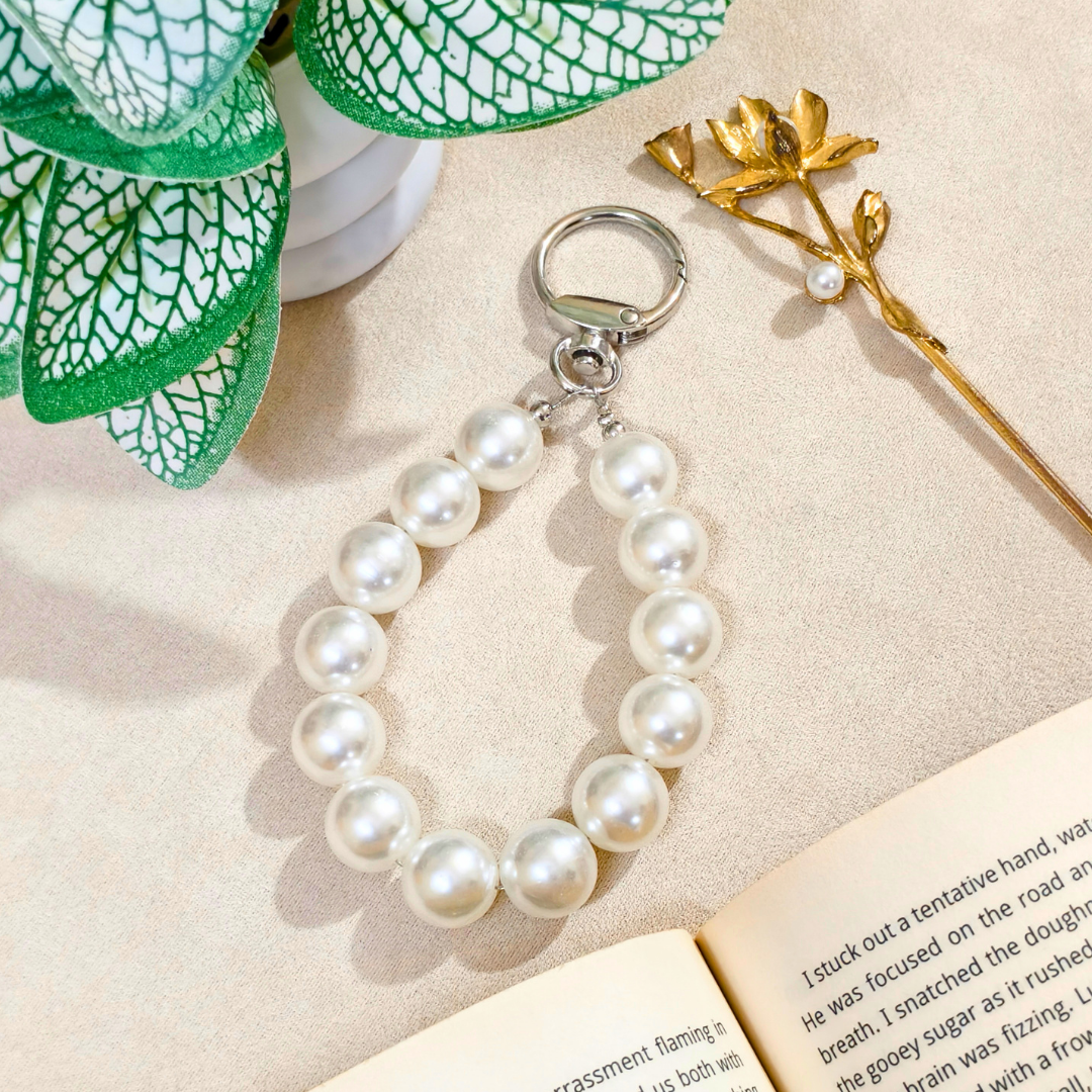 Pearl bracelet keychain on a textured surface with a book and decorative elements.