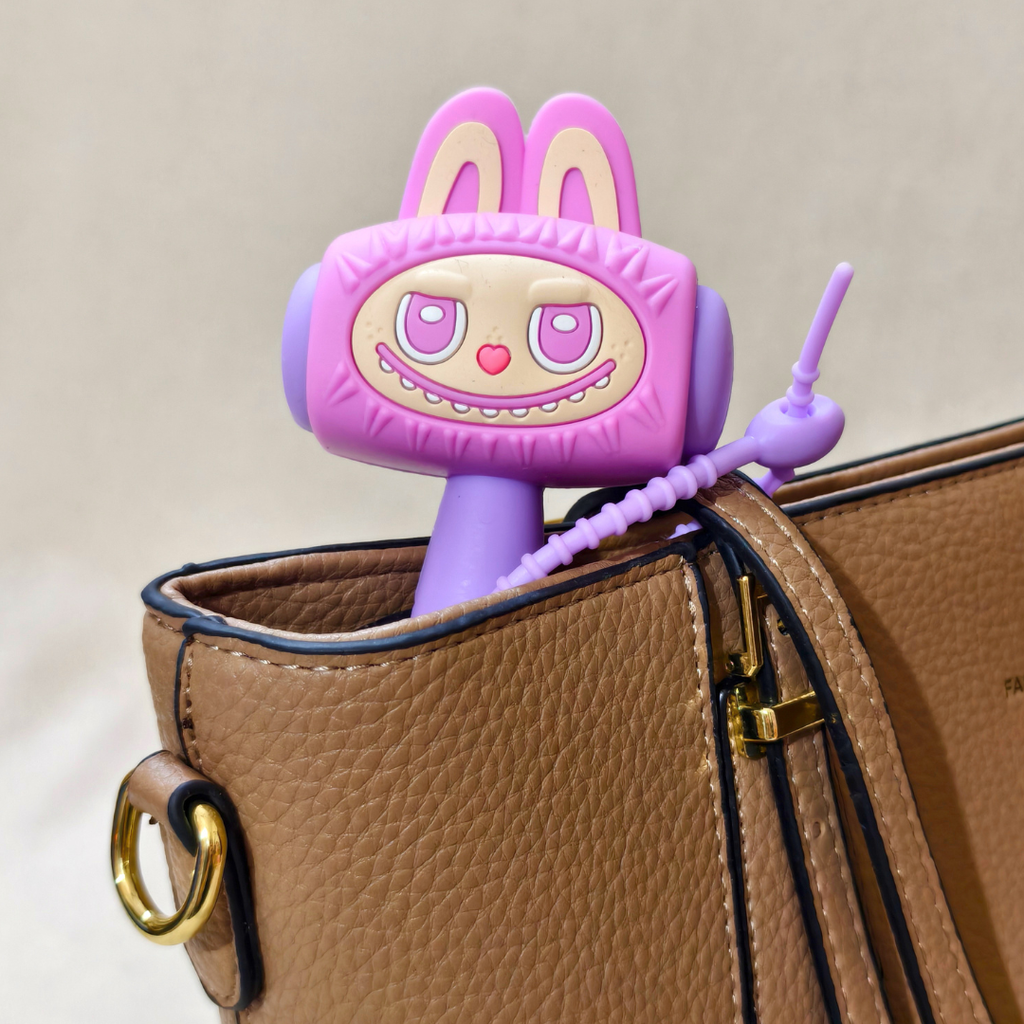 A purple and pink cartoon rabbit-shaped accessory with long ears and a beaded arm, partially tucked into a brown textured handbag.