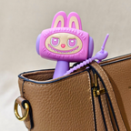 A purple and pink cartoon rabbit-shaped accessory with long ears and a beaded arm, partially tucked into a brown textured handbag.
