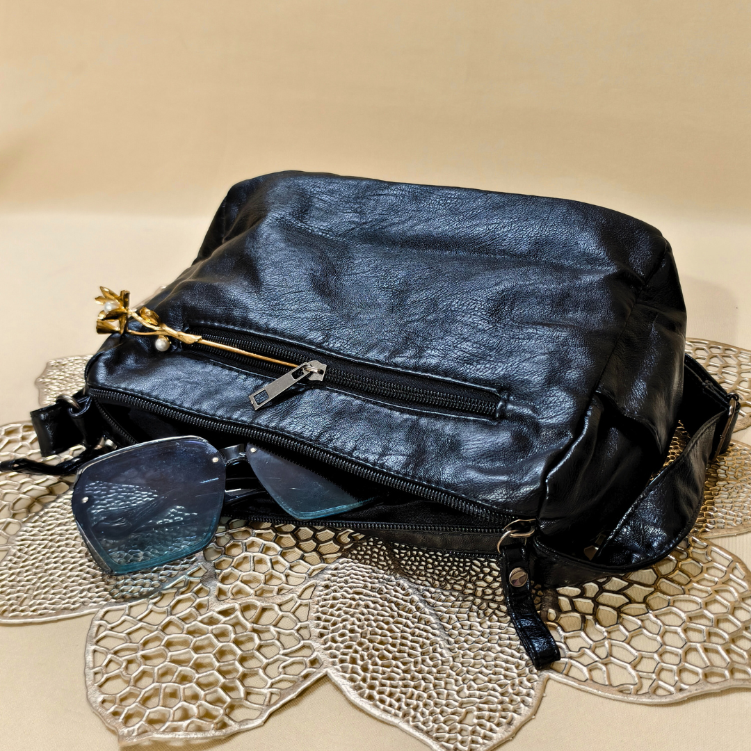 Black leather bag with sunglasses on a textured surface