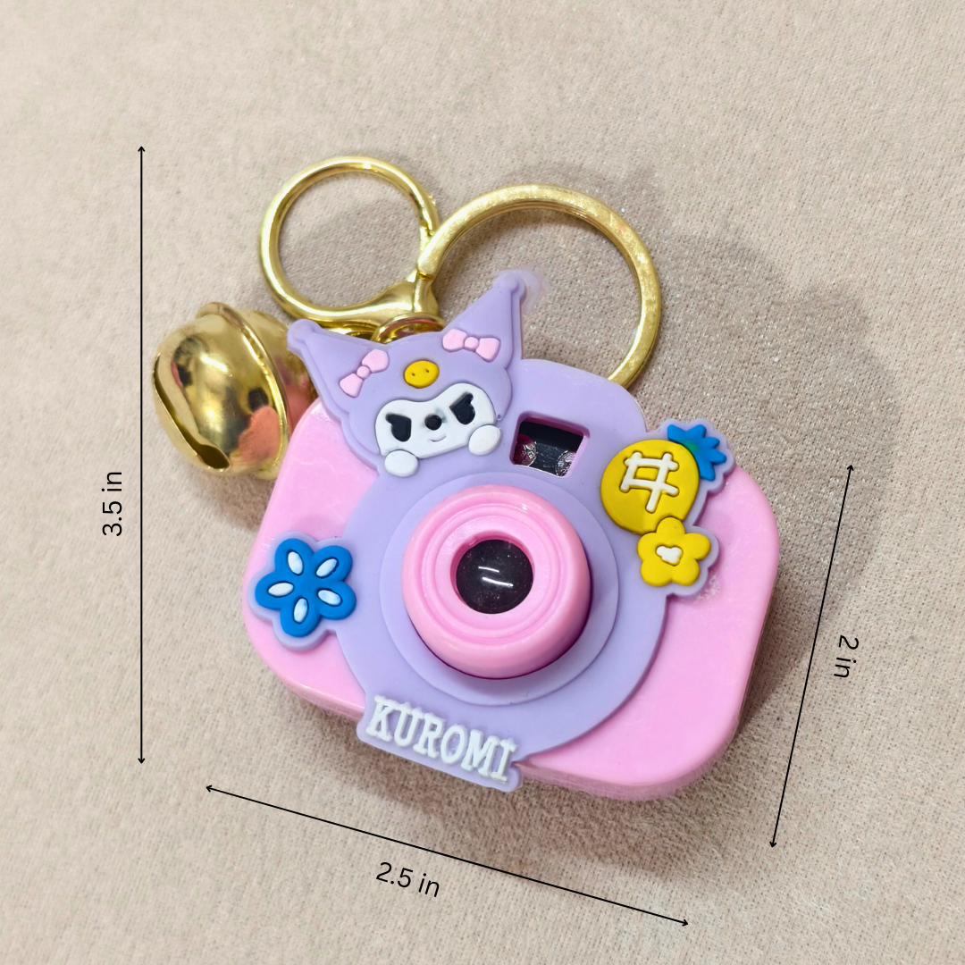 Pink camera-shaped keychain with cartoon character and bell, measurements indicated on a beige background