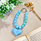 Blue heart-shaped keychain on a beige surface with flowers and a book