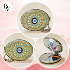 Oval compact mirror keychain with a colorful mandala pattern and blue evil eye design, shown closed and open on a soft pink background.