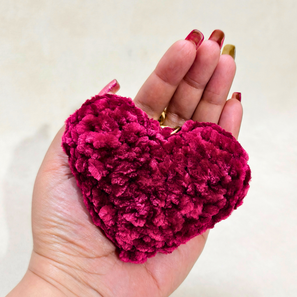 Hand holding a pink heart-shaped plush toy against a white background