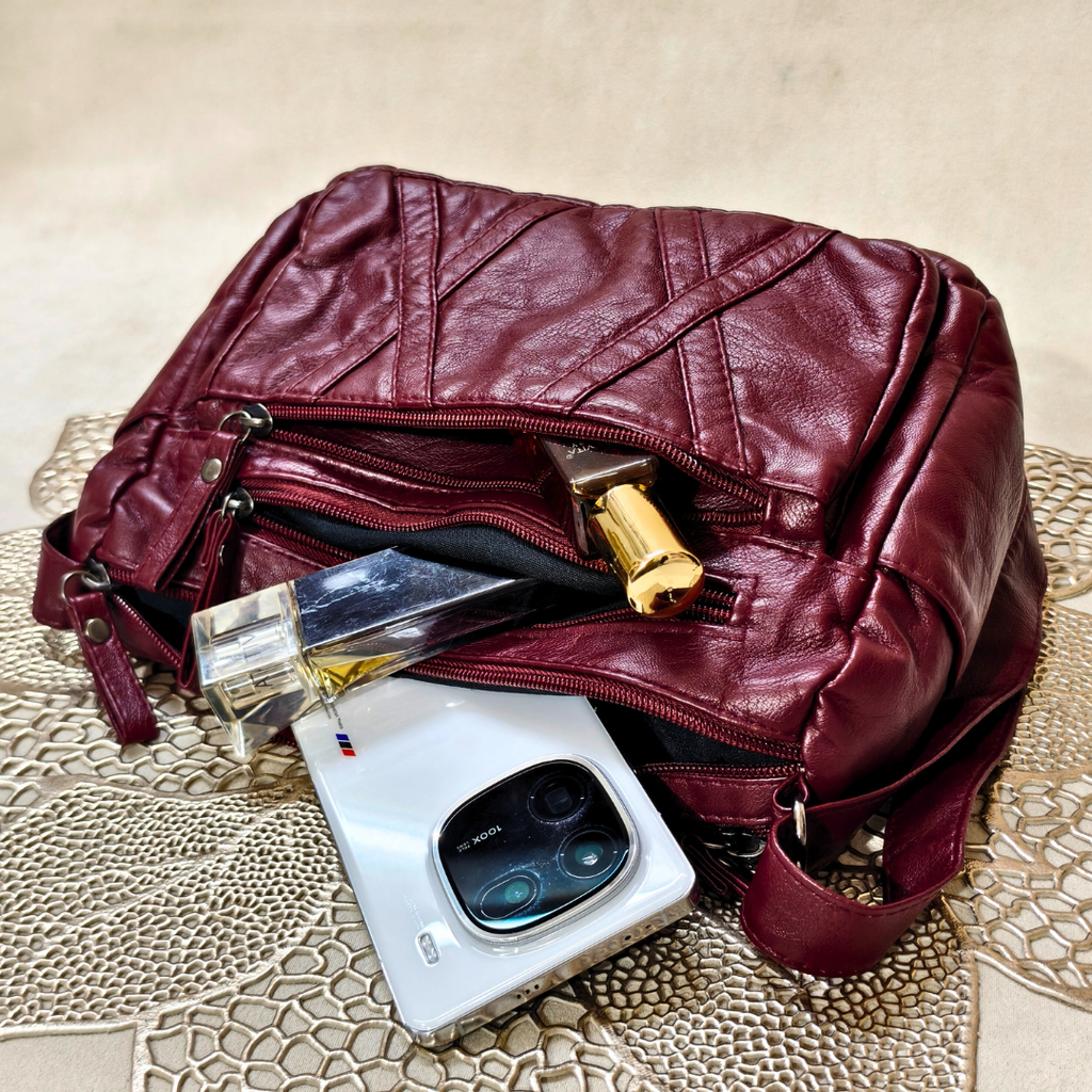 Maroon leather handbag with a phone, perfume bottle, and wallet on a textured surface