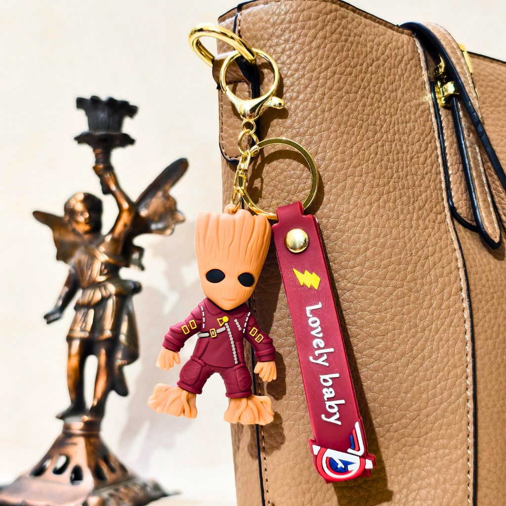 Groot keychain with a 'Lovely baby' tag attached to a brown bag, with a bronze statue in the background.