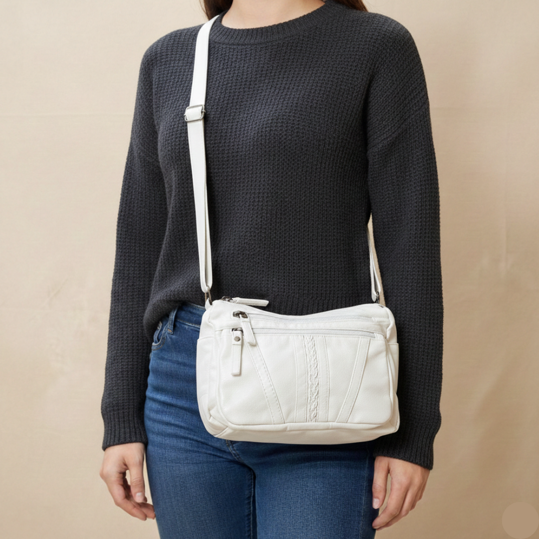 Person wearing a dark sweater and blue jeans with a white crossbody bag on a beige background