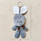 Gray plush bunny keychain with a brown bow on a beige background, showing measurements.