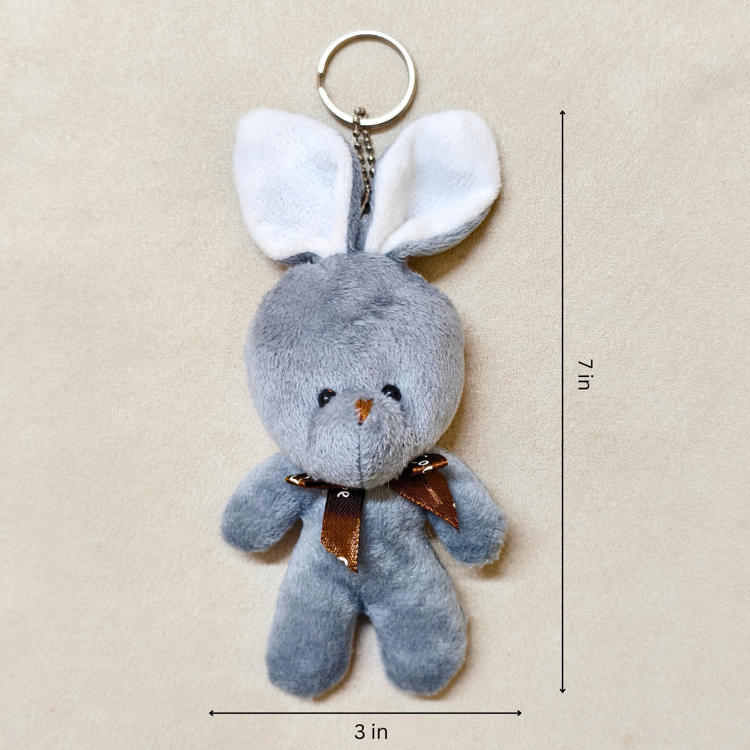 Gray plush bunny keychain with a brown bow on a beige background, showing measurements.