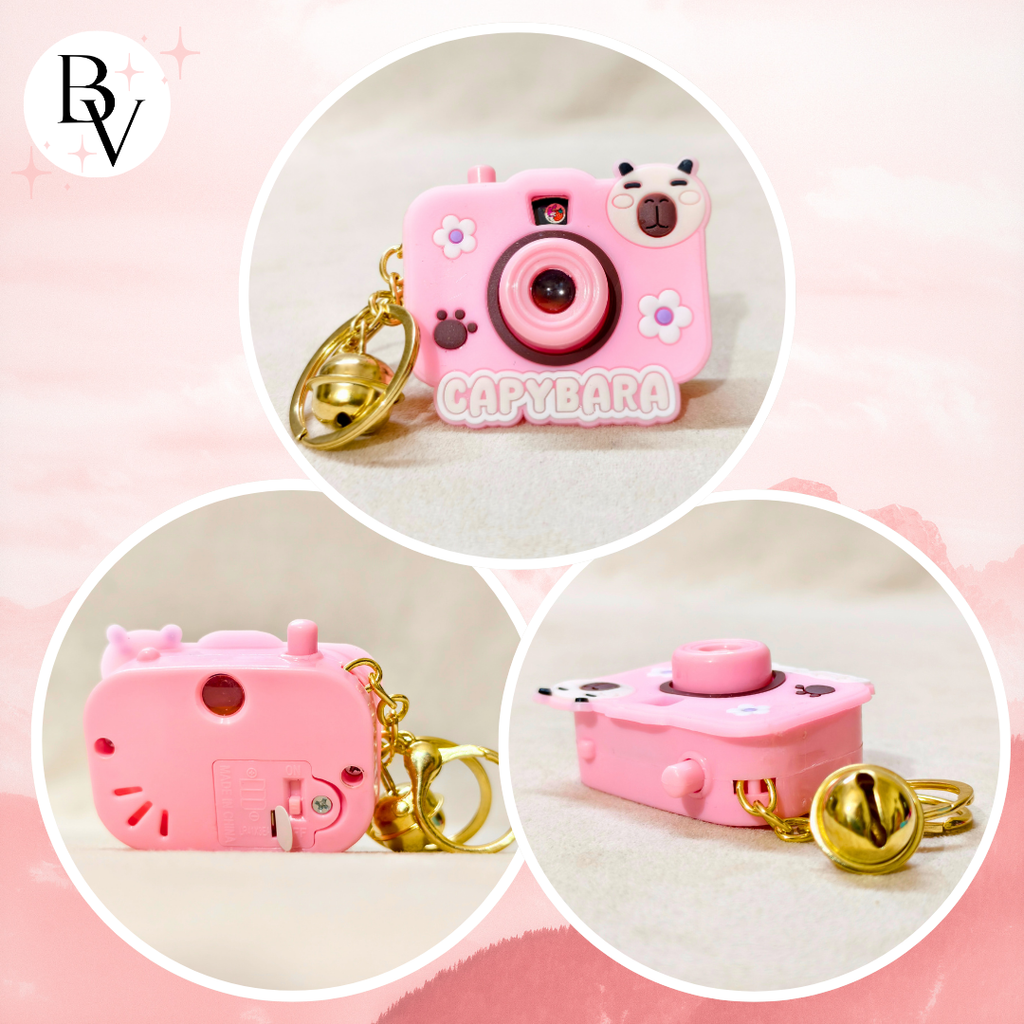 Pink capybara-shaped camera keychain with bell on a pink background
