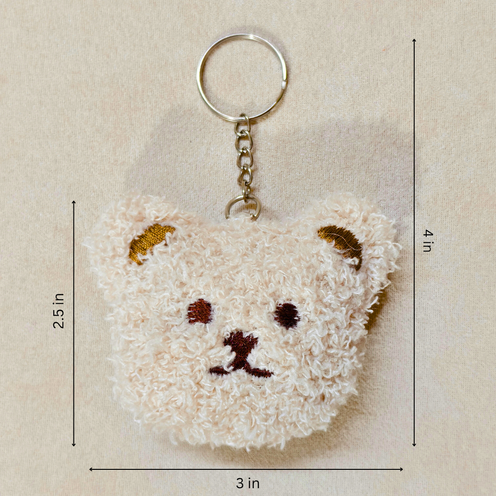 A plush teddy bear face keychain with a gold metal key ring and chain, shown on a beige textured background with dimension lines indicating 3 in width, 2.5 in height, and 4 in overall size.