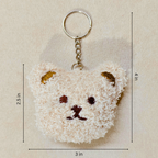 A plush teddy bear face keychain with a gold metal key ring and chain, shown on a beige textured background with dimension lines indicating 3 in width, 2.5 in height, and 4 in overall size.