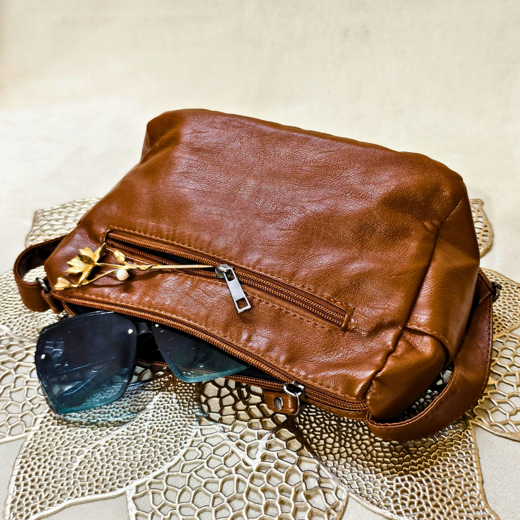 Brown leather bag with sunglasses on a textured surface