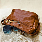 Brown leather bag with sunglasses on a textured surface