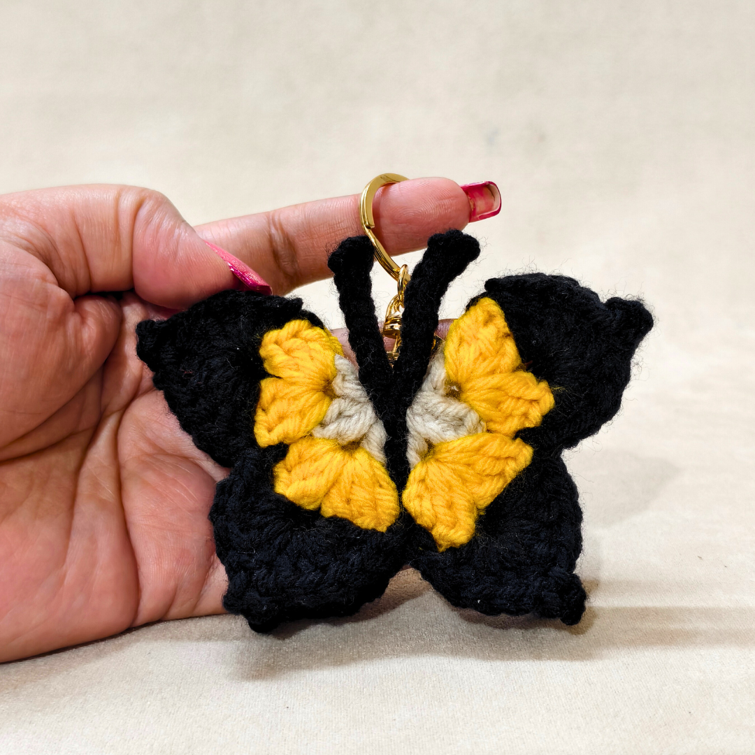 Hand holding a black and yellow butterfly keychain against a neutral background