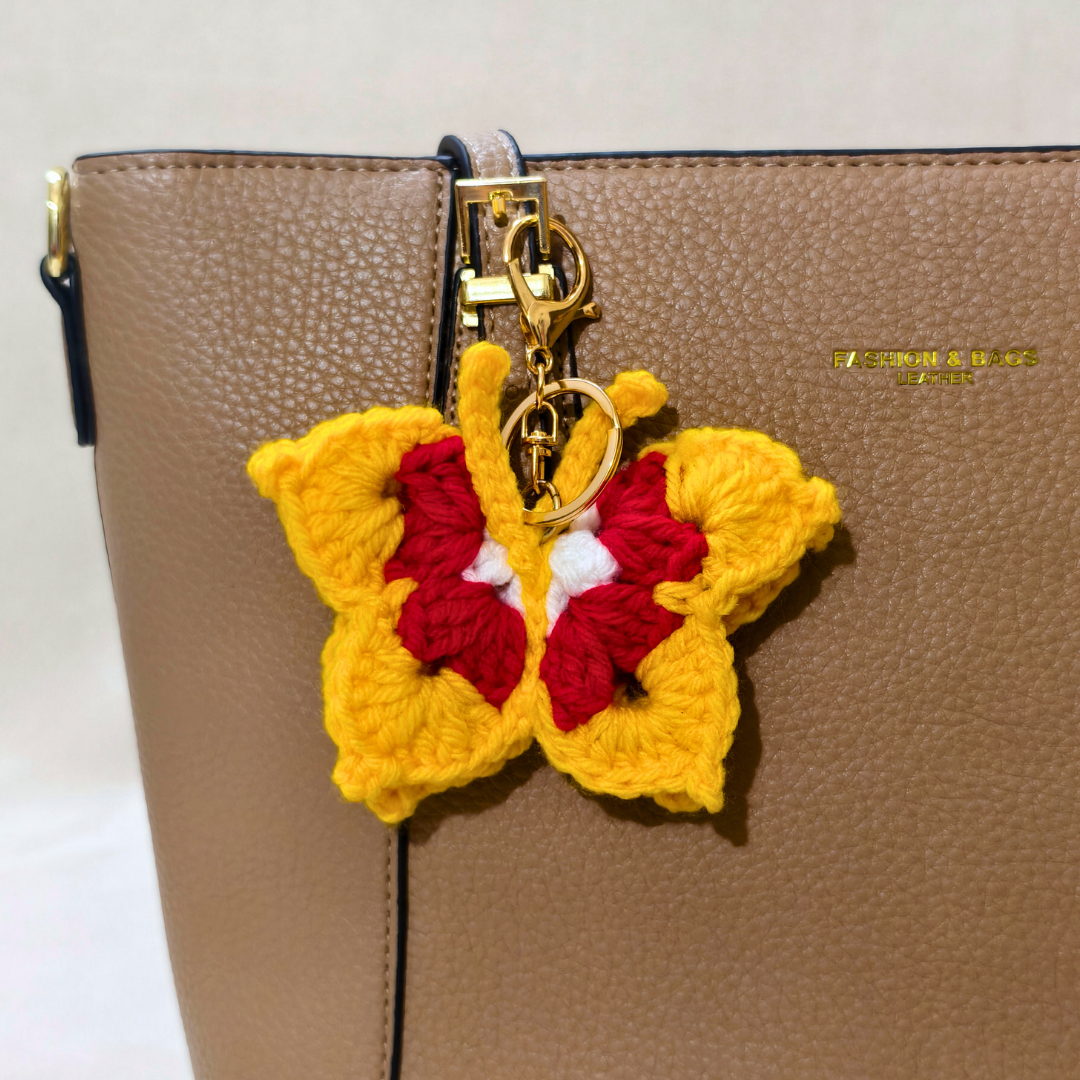 Yellow Red Butterfly Crochet Bag Charm Attached On Handbag In Front Of Beige Background