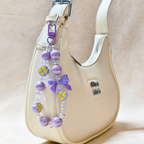 Lilac Bow Charm Attached On Hand Bag In The Front Of Beige Background.