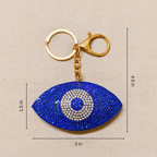 Blue eye-shaped keychain with gold clasp on beige background