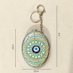 An oval keychain holder with a colorful mandala pattern and a blue-and-white evil eye in the center, shown on a beige background with dimension lines indicating 3.5 in height, 6 in overall height, and 2.