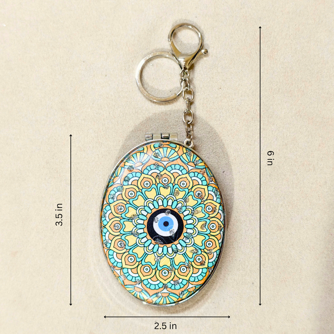 An oval keychain holder with a colorful mandala pattern and a blue-and-white evil eye in the center, shown on a beige background with dimension lines indicating 3.5 in height, 6 in overall height, and 2.