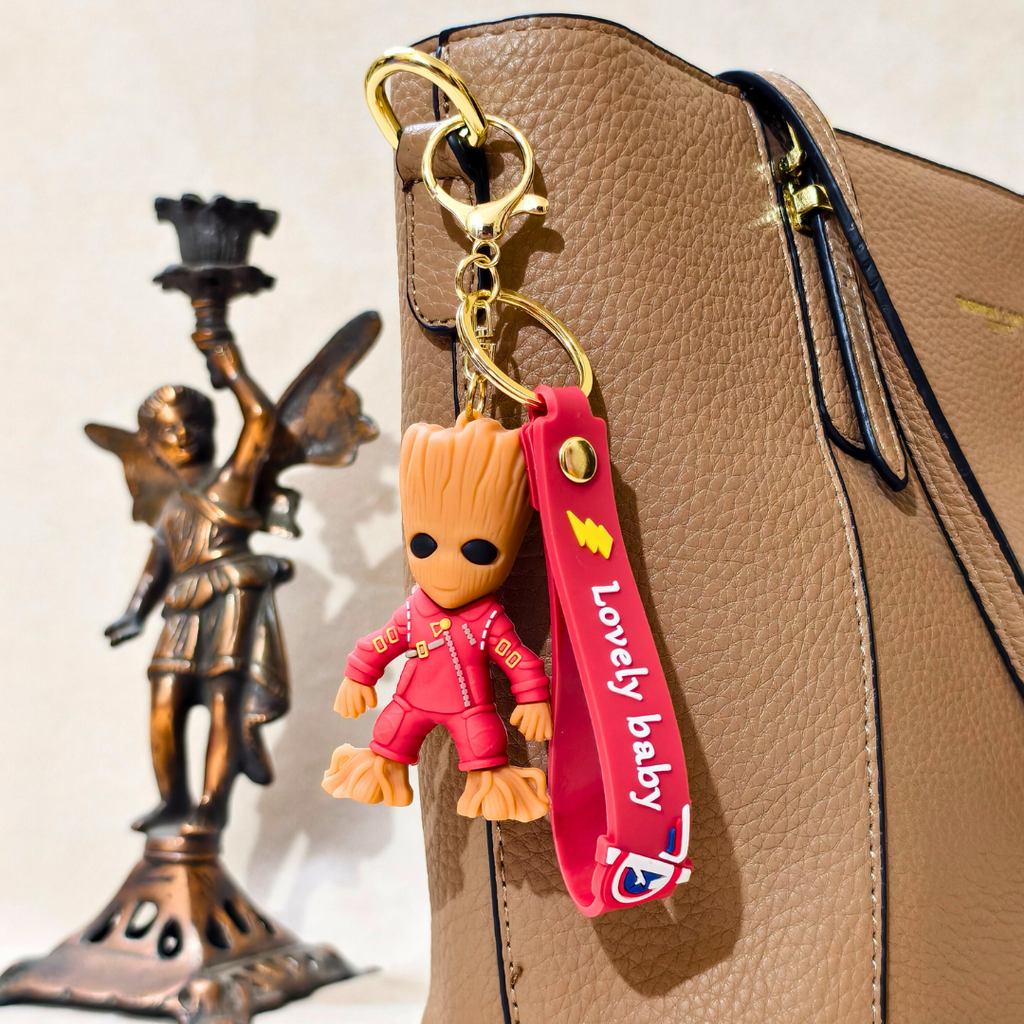 Keychain with a small figurine attached to a bag, featuring a gold angel statue in the background.