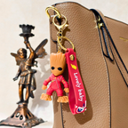 Keychain with a small figurine attached to a bag, featuring a gold angel statue in the background.