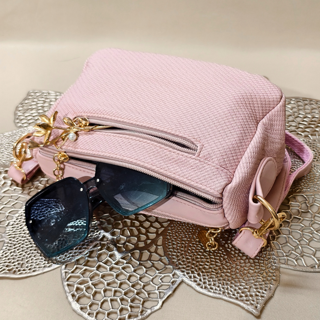 Pink handbag with gold accents and sunglasses on a textured surface