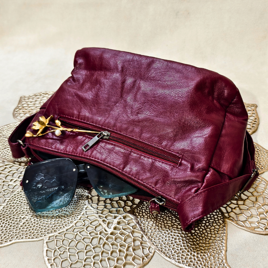 Maroon leather bag with sunglasses on a textured surface