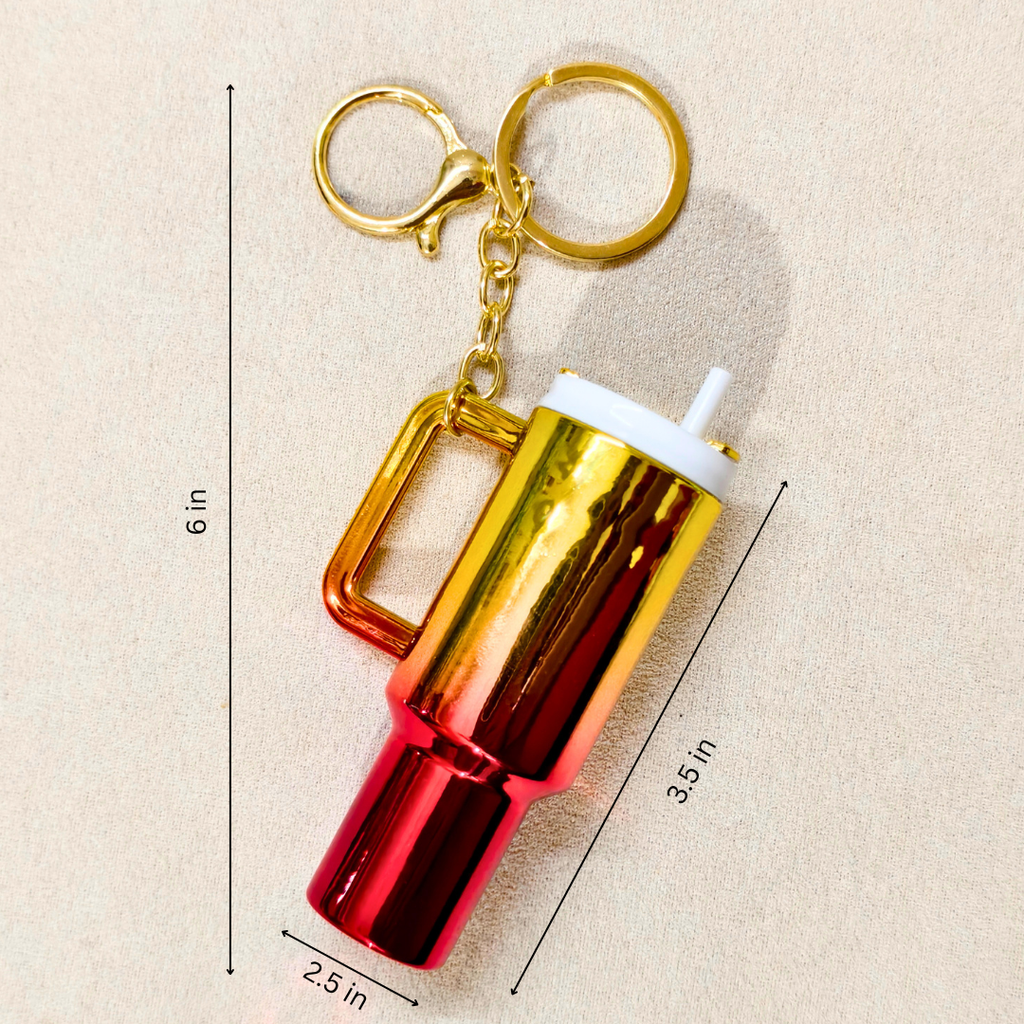 A metallic keychain tumbler with a gold-to-red gradient body, a gold handle, and a white straw, shown on a beige background with dimension lines indicating 6 in height, 3.5 in width, and 2.