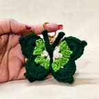 Hand holding a green and white crocheted butterfly keychain against a beige background