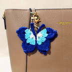 Blue and white butterfly-shaped keychain attached to a beige handbag.