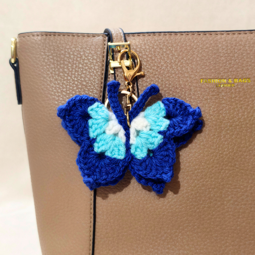 Blue and white butterfly-shaped keychain attached to a beige handbag.