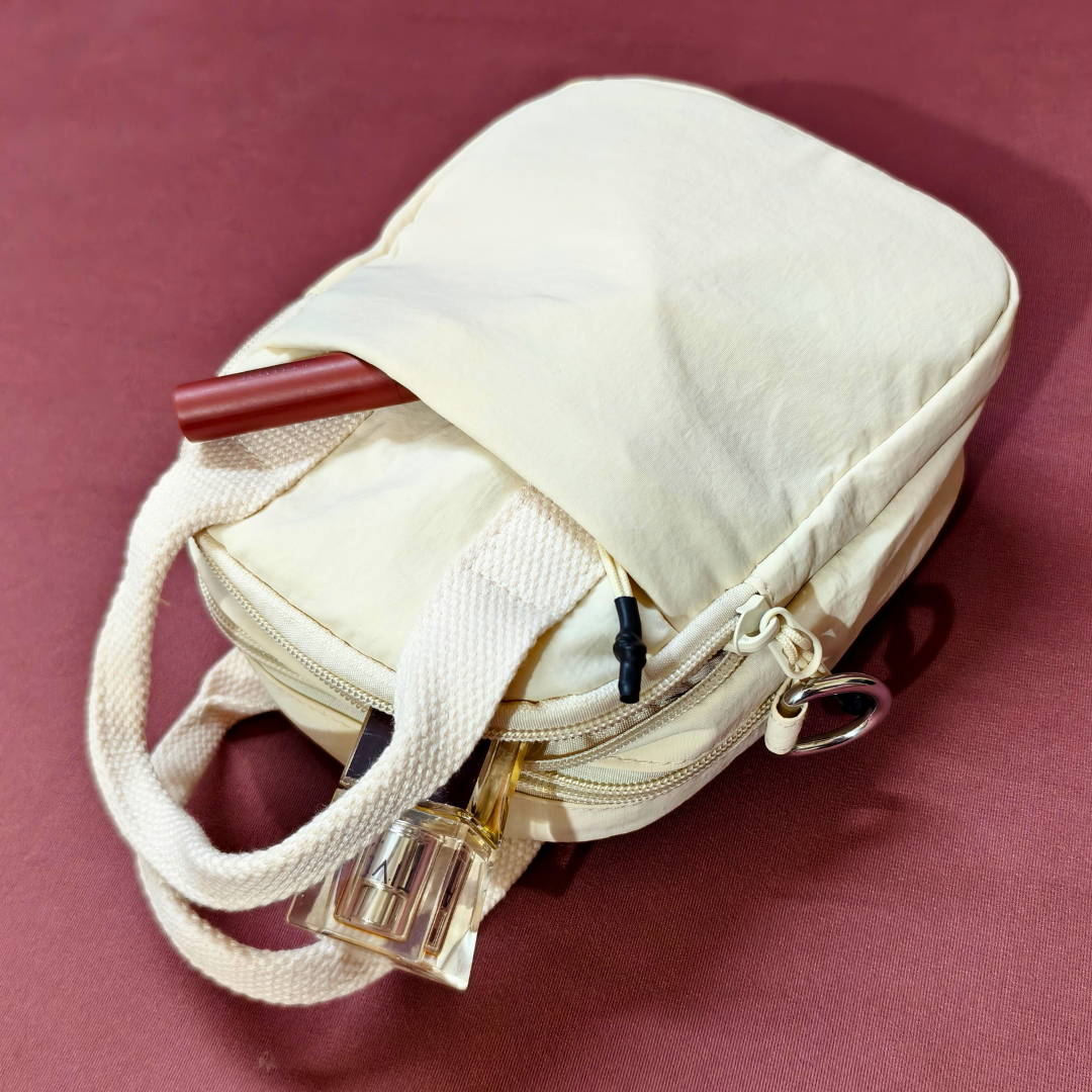 Beige makeup bag with a lip pencil and perfume bottle on a maroon background
