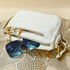 White handbag with gold accents and blue sunglasses on a textured surface