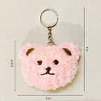 A pink fuzzy teddy bear keychain with a metal key ring and chain, shown on a light beige textured background with dimension lines and labels indicating 3 in width, 2.5 in height, and 4 in overall height.