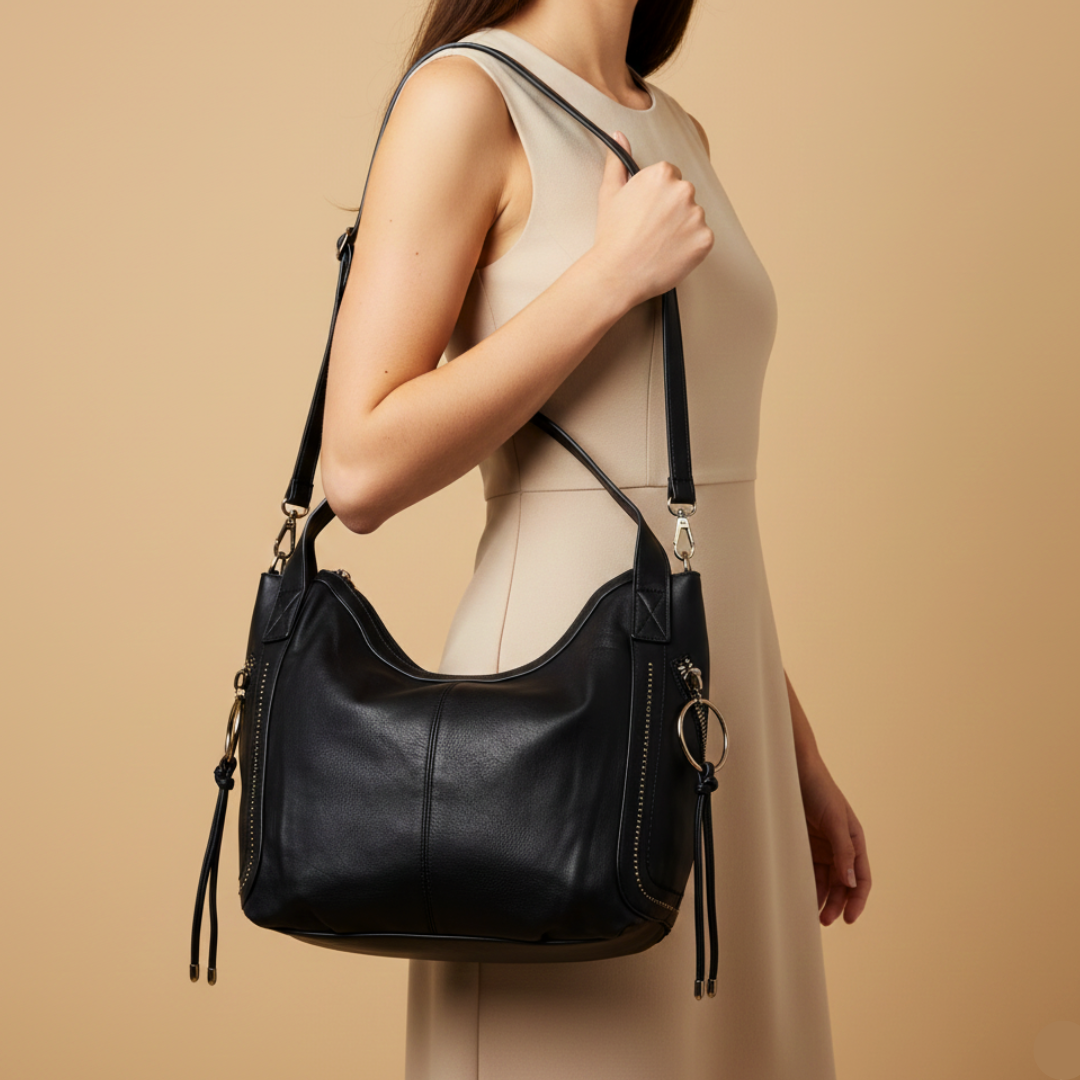 Black leather handbag held by a person against a beige background