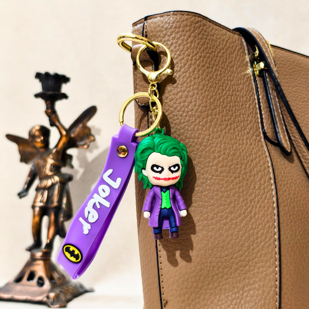 Joker keychain with a purple strap on a brown leather bag, with a statue in the background.