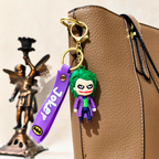 Joker keychain with a purple strap on a brown leather bag, with a statue in the background.