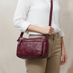 Person holding a burgundy leather handbag against a neutral background