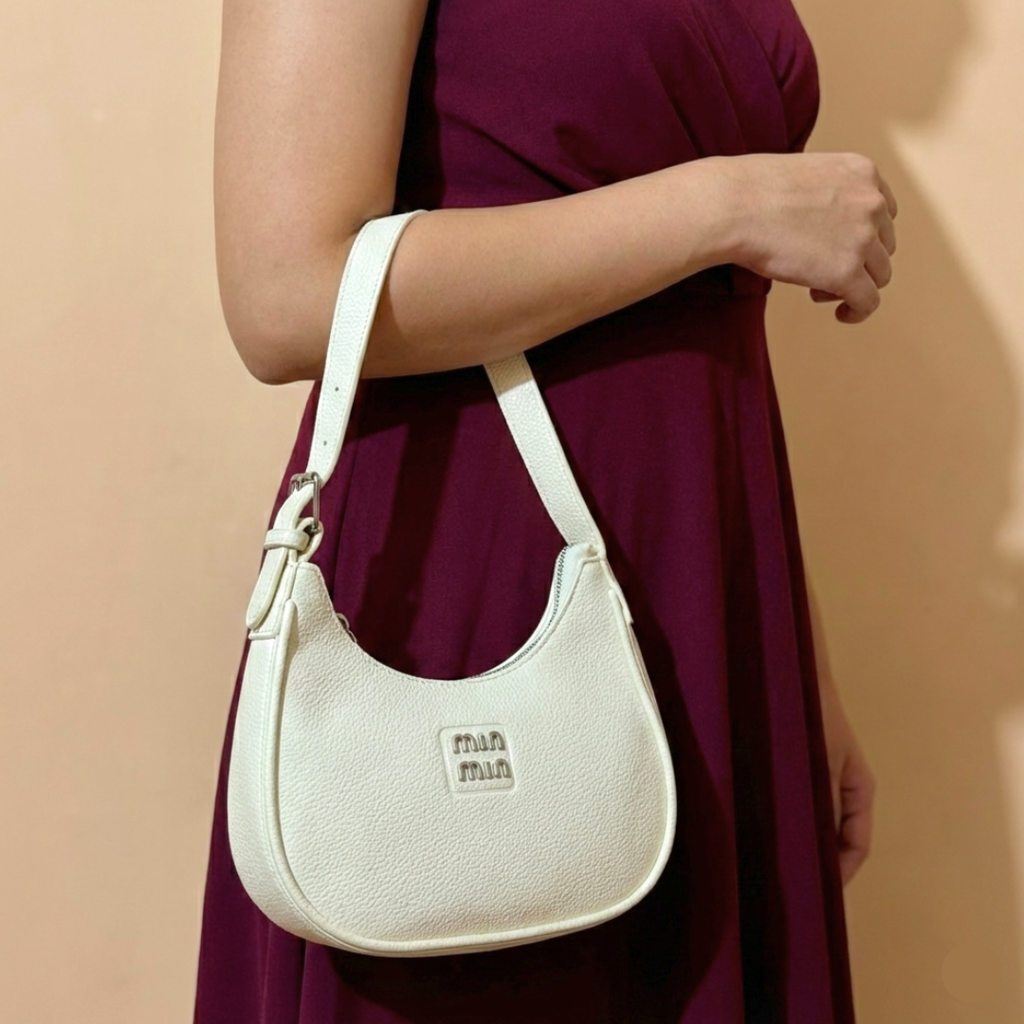 Woman holding a white handbag with 'mim' logo against a beige background