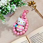 Pink character keychain with beads on a beige surface with flowers and an open book.