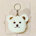 A white fluffy teddy bear face charm with brown ears, nose, and eyes, hanging from a silver-tone ring showing measurement on a beige background.