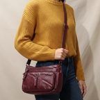 Person wearing a mustard yellow sweater with a burgundy handbag on a plain background