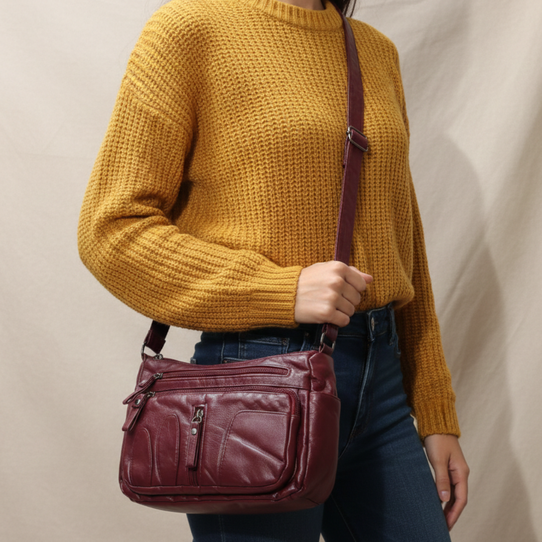 Person wearing a mustard yellow sweater with a burgundy handbag on a plain background