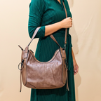 Person wearing a green dress holding a brown leather handbag against a beige background