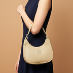 Beige handbag held by a person wearing a navy dress on a brown background