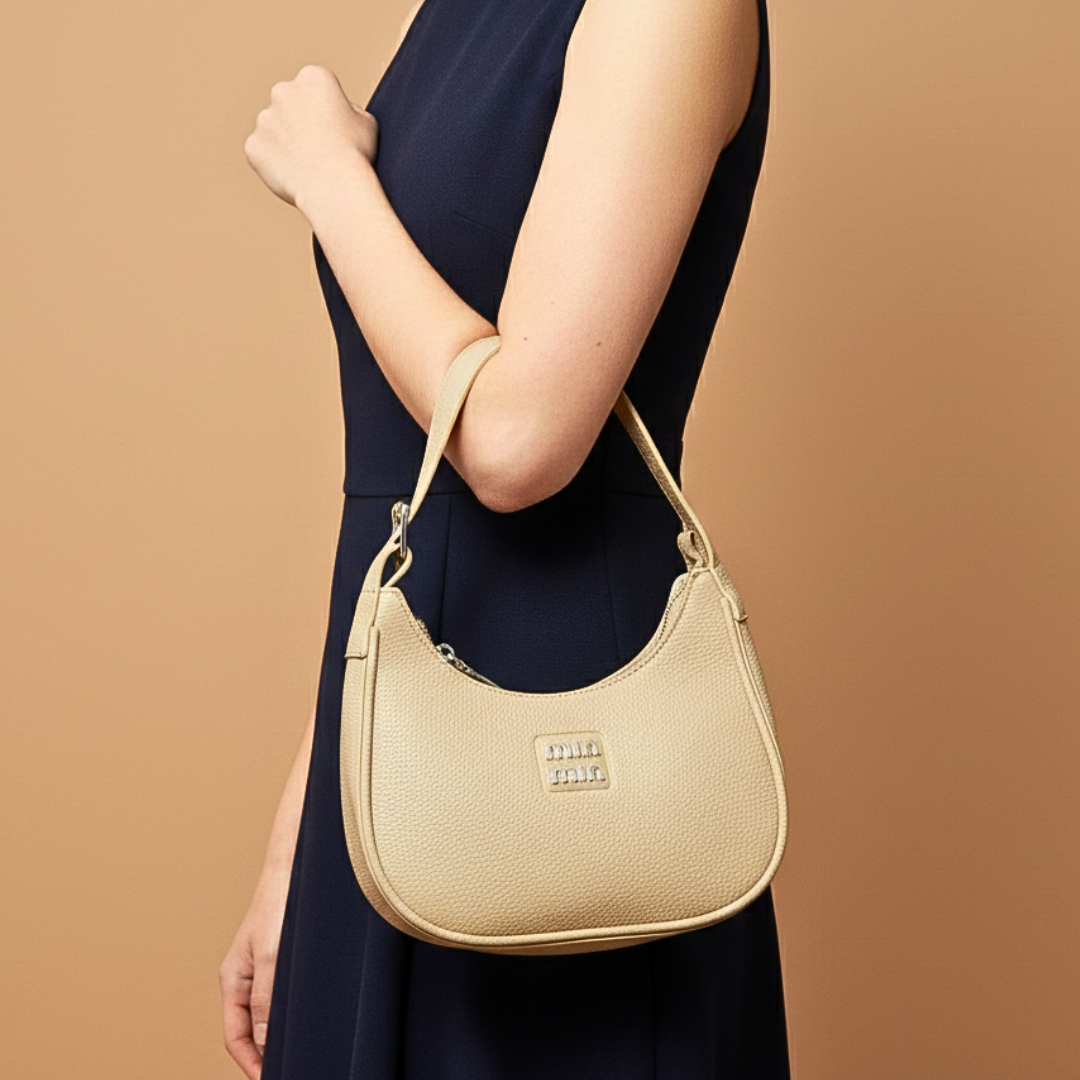 Beige handbag held by a person wearing a navy dress on a brown background