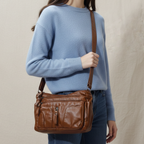 Person wearing a blue sweater holding a brown leather bag against a beige background